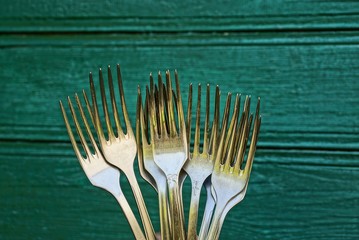 Набор металлических вилок на фоне зелёной деревянной стены