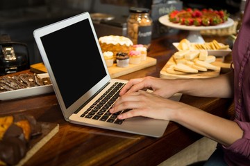 Woman using laptop at bakery counter in market