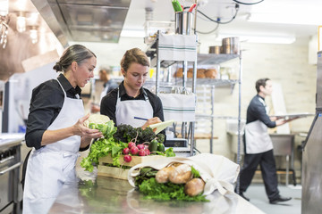Female chefs examining vegetables while male coworker working in background