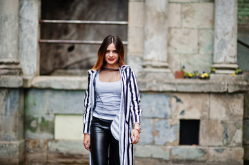 Fashionable woman look with black and white striped suit jacket, leather pants,  posing at old street. Concept of fashion girl.