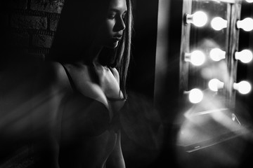 Black-and-white photo of a young girl standing amid the lamps in black lingerie.