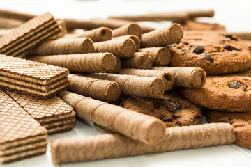 Chocolate waffle rolls, biscuits and classic waffle on a wooden white table. Fresh sweets.