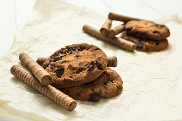 Two slides of chocolate waffle rolls, cookies on a wooden white table.