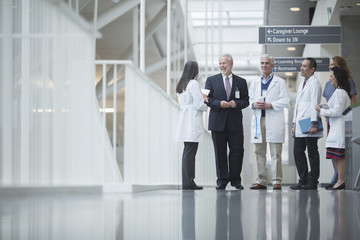 Senior doctor discussing with coworkers while standing in hospital corridor