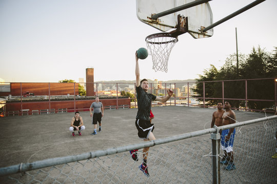 Friends looking at man dunking while practicing basketball in court