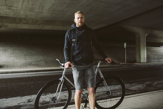Portrait of confident male commuter standing by bicycle on bridge