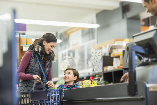 Smiling woman holding basket while standing with son by checkout counter at supermarket