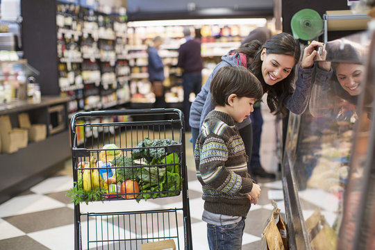 Smiling woman looking at son standing by display cabinet in supermarket