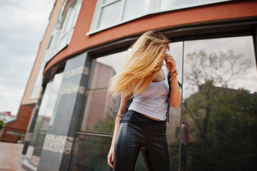 Fashionable woman look at white shirt, black transparent clothes, leather pants, posing at street against large windows of building. Concept of fashion girl.