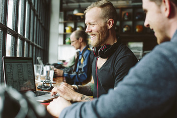 Male colleagues working on laptop at desk in office
