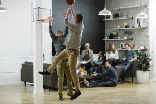 Businessmen playing basketball while colleagues sitting in background at office