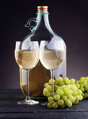 Bottle and glass of white wine, grape on wooden table