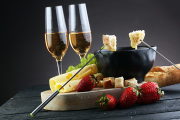 Gourmet Swiss fondue dinner with assorted cheeses on a board and strawberries alongside a heated...