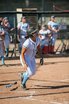 Latina softball player watching her fly ball as bat drops