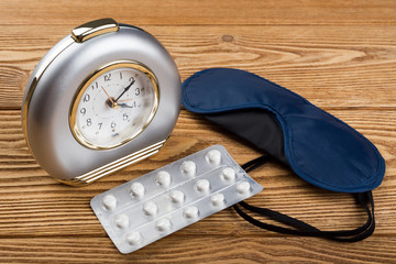 Alarm clock, mask and sleeping pills on a wooden background 