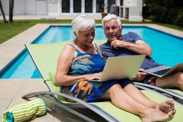 Senior couple using laptop on lounge chair