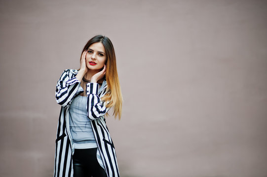 Fashionable woman look with black and white striped suit jacket, leather pants posing against wall. Concept of fashion girl.