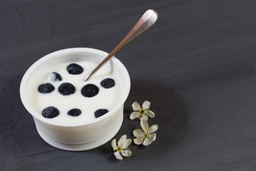 Yogurt with fresh blueberries, and several flowers beside on black background