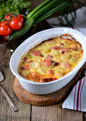 Potato casserole with sausages, onions and cheese on an old wooden background. Rustic style.