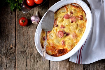 Potato casserole with sausages, onions and cheese on an old wooden background. Rustic style.