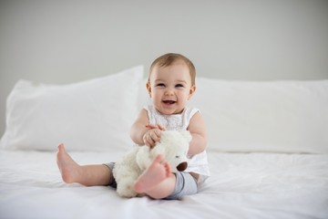 Cute baby girl playing with soft toy on bed - obrazy, fototapety, plakaty