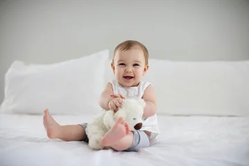 Fototapeten Cute baby girl playing with soft toy on bed © WavebreakMediaMicro