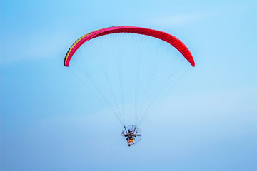 Rear view of man flying with paramotor glider parachute on beautiful blue sky