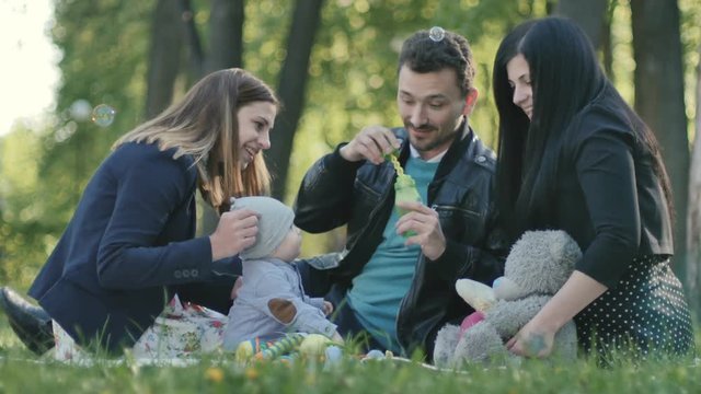 Swedish family with little son blow bubbles on a coverlet in park
