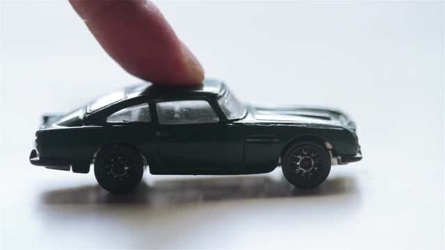 closeup sideview of a green toy car being pushed by a finger and hitting another pink one out of the frame