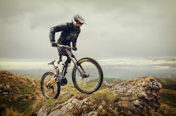 Ryder in full protective equipment on the mtb bike climbs on a rock against the backdrop of a...
