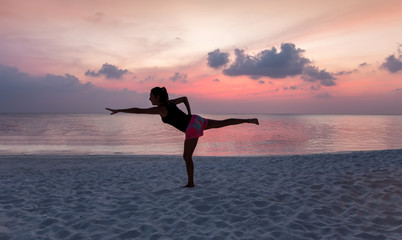 Frau beim Yoga am tropischen Strand bei Sonnenuntergang