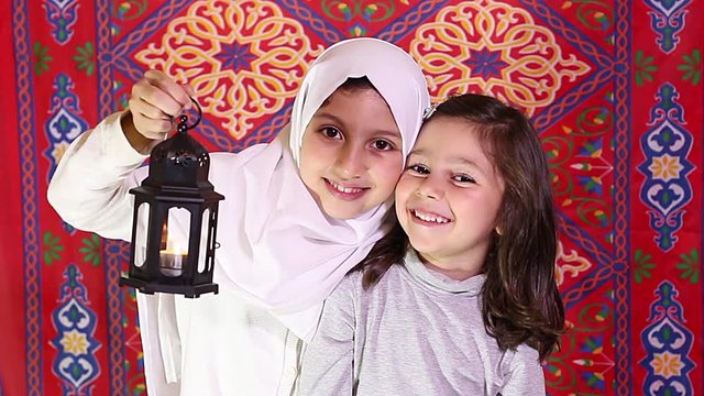 Happy Family in Ramadan - Two Muslim sisters celebrating Ramadan - playing with Ramadan lantern in front of Ramadan background