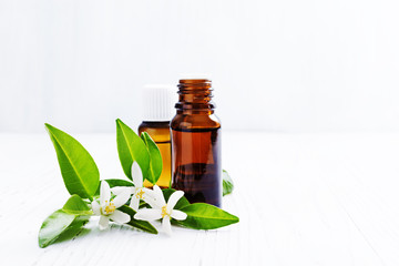 Neroli (Citrus aurantium) essential oil in a brown glass bottle with fresh white  flowers on ligth...