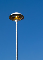 Tall light (in a supermarket car park)  switched on even though it is bright daylight.