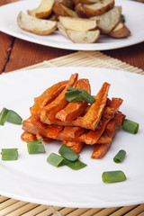 Baked carrots and potatoes with green onions on a white plate. Organic Vegetarian Food on a bamboo mat