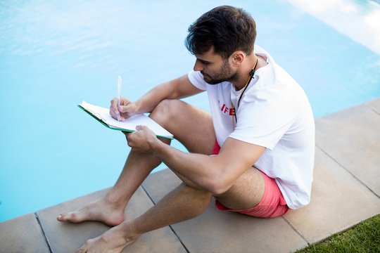 Lifeguard writing on clipboard at poolside - Powered by Adobe