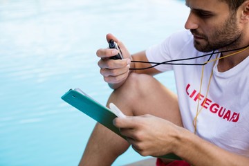 Lifeguard holding clipboard and stopwatch at poolside - Powered by Adobe