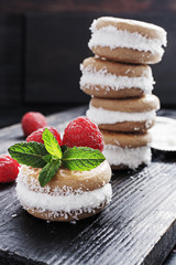 Homemade ice cream sandwiches  with coconut flakes raspberries and mint on old black wooden board, over marble texture background. Top view with copy space.