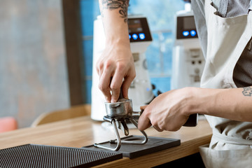 Closer look. Cropped closeup of a barista pressing ground using a tamper