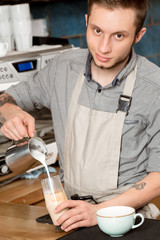 Careful professionalism. Vertical portrait of a young barista pouring milk into coffee looking to the camera