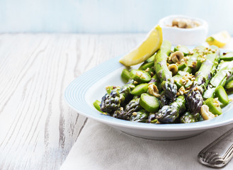 Warm salad with asparagus, hazelnuts and lemon on old white wooden surface,selective focus, close up.