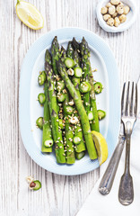 Warm salad with asparagus, hazelnuts and lemon on old white wooden surface, top view.