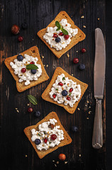 Open toast  sandwiches with fresh berries blueberry and pomegranate, cottage cheese, thyme and hazelnuts, served with vintage knife over old dark wooden textured board. Top view
