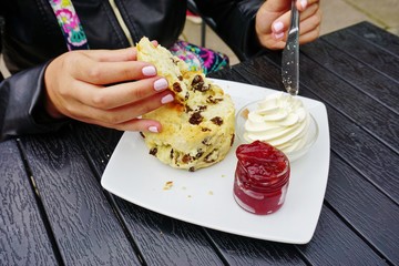 Eating a currant scone with strawberry jam and clotted cream