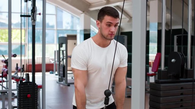 Muscular man working out in gym doing exercises at triceps.