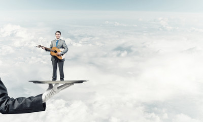 Fototapeta na wymiar Businessman on metal tray playing acoustic guitar against blue sky background