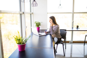 Entrepreneur calling on phone and working on line with a laptop sitting in a desk at office