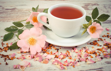 Vintage photo, Cup of tea with wild rose flower on old rustic board