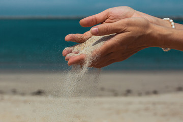 Sand pours through fingers against the sea.