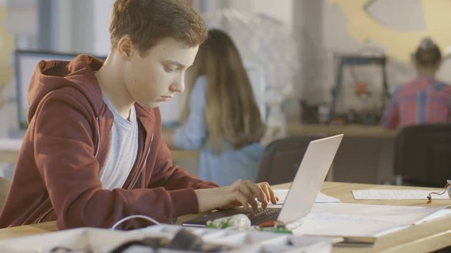 Smart Bot Uses Laptop at School Working on a Project Writing Paper.Shot on RED EPIC-W 8K Helium Cinema Camera.